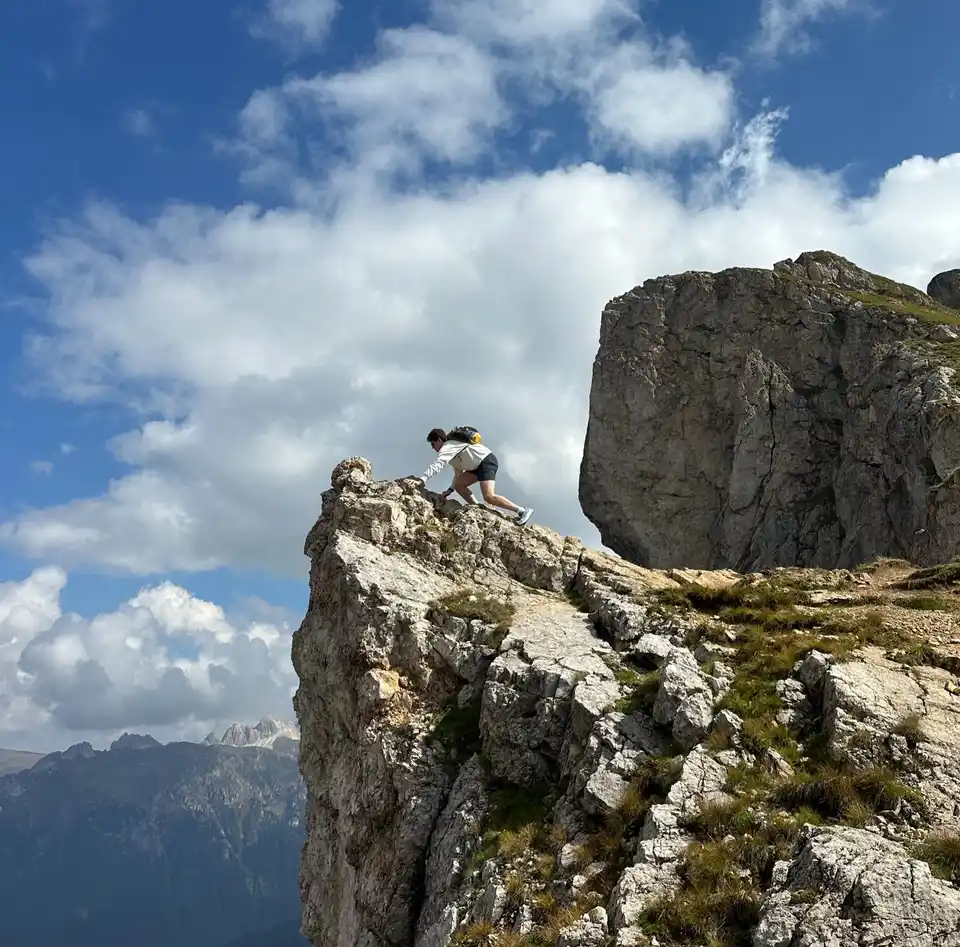 A hiker climbs onto the top of a tall rocky cliff under blue sky.