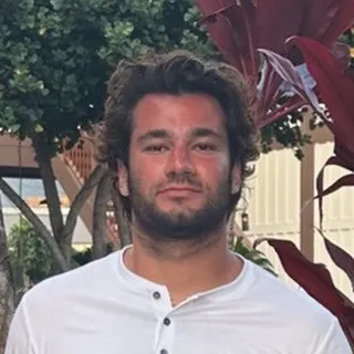 A PWP coaching client and grad student standing outdoors in a white henley shirt.