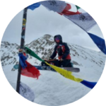 female snowboarder on top of snowy mountain with summit flags in foreground